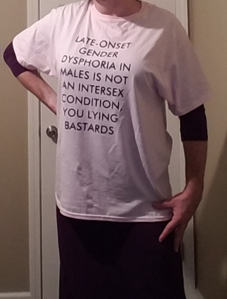 torso shot of crossdressed male wearing "LATE ONSET GENDER DYSPHORIA IN MALES IS NOT AN INTERSEX CONDITION" T-shirt over purple dress